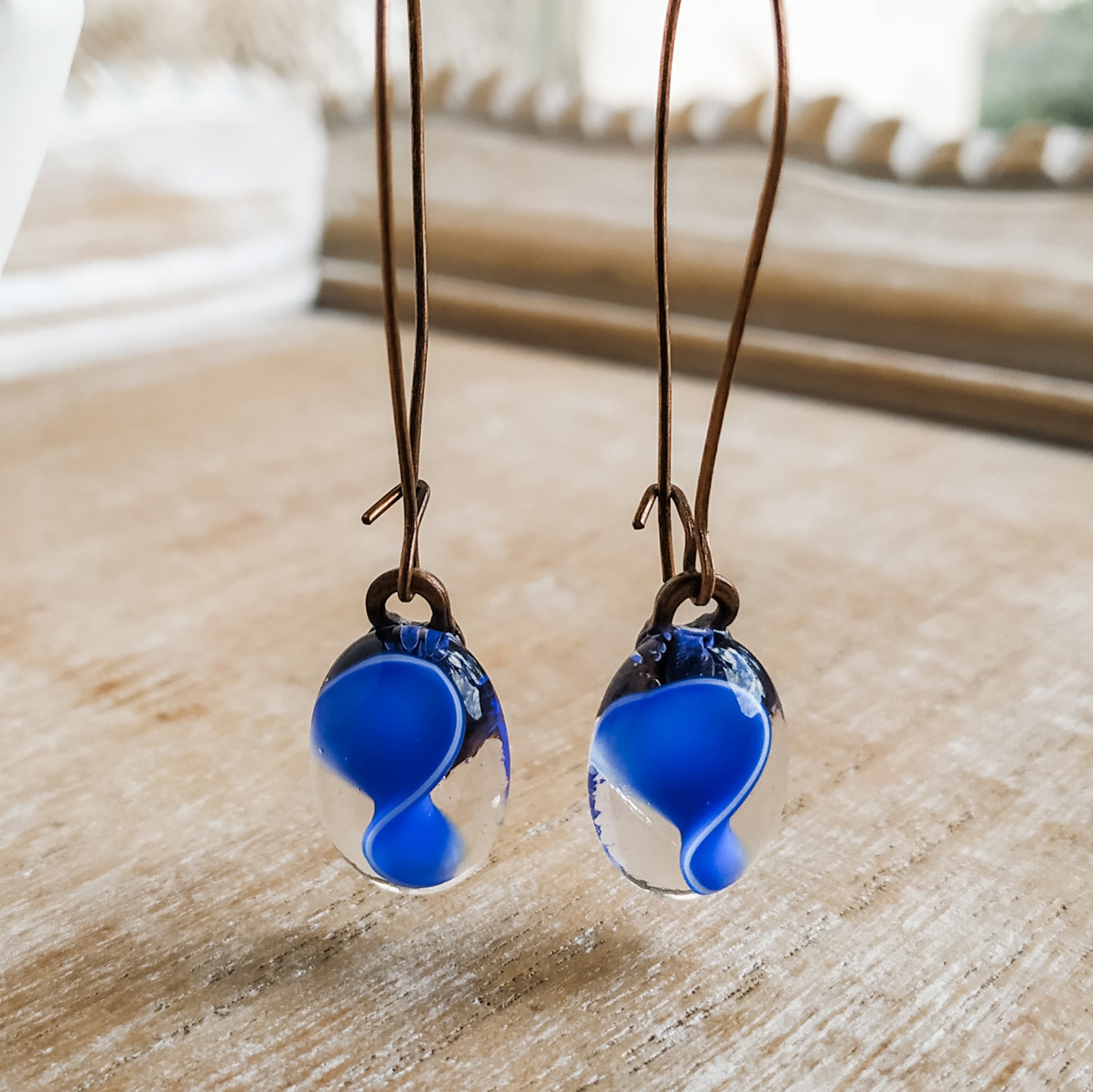 Blue earrings hanging in front of window. handmade by Pamela Angus 