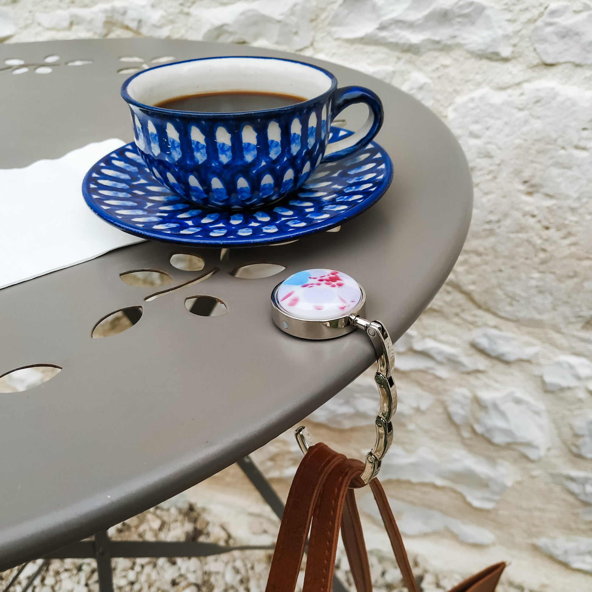 Coffee cup and saucer on bistro table with bag hanger and handbag