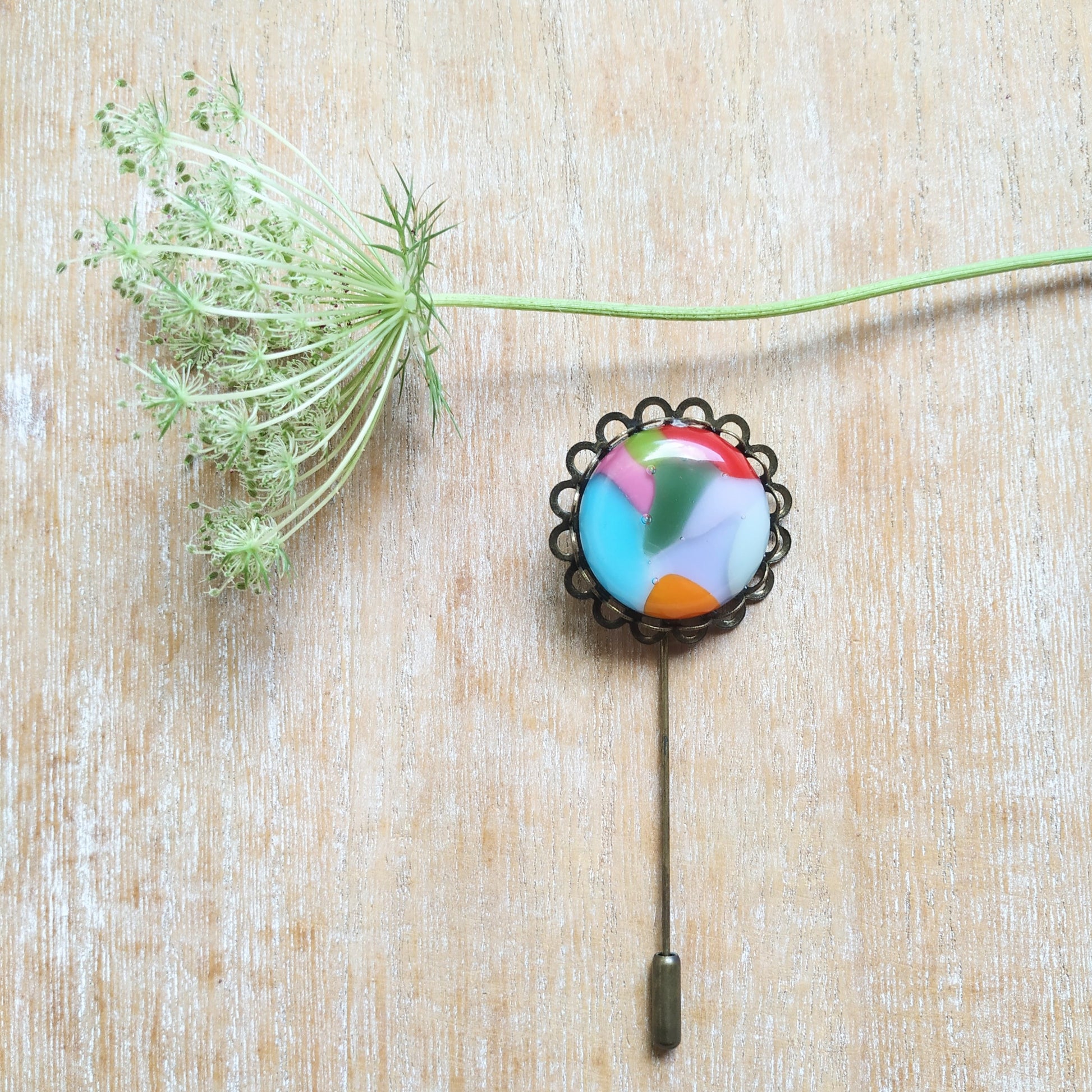 Colorful brooch and  wild flower on table. Handmade by Pamela Angus 